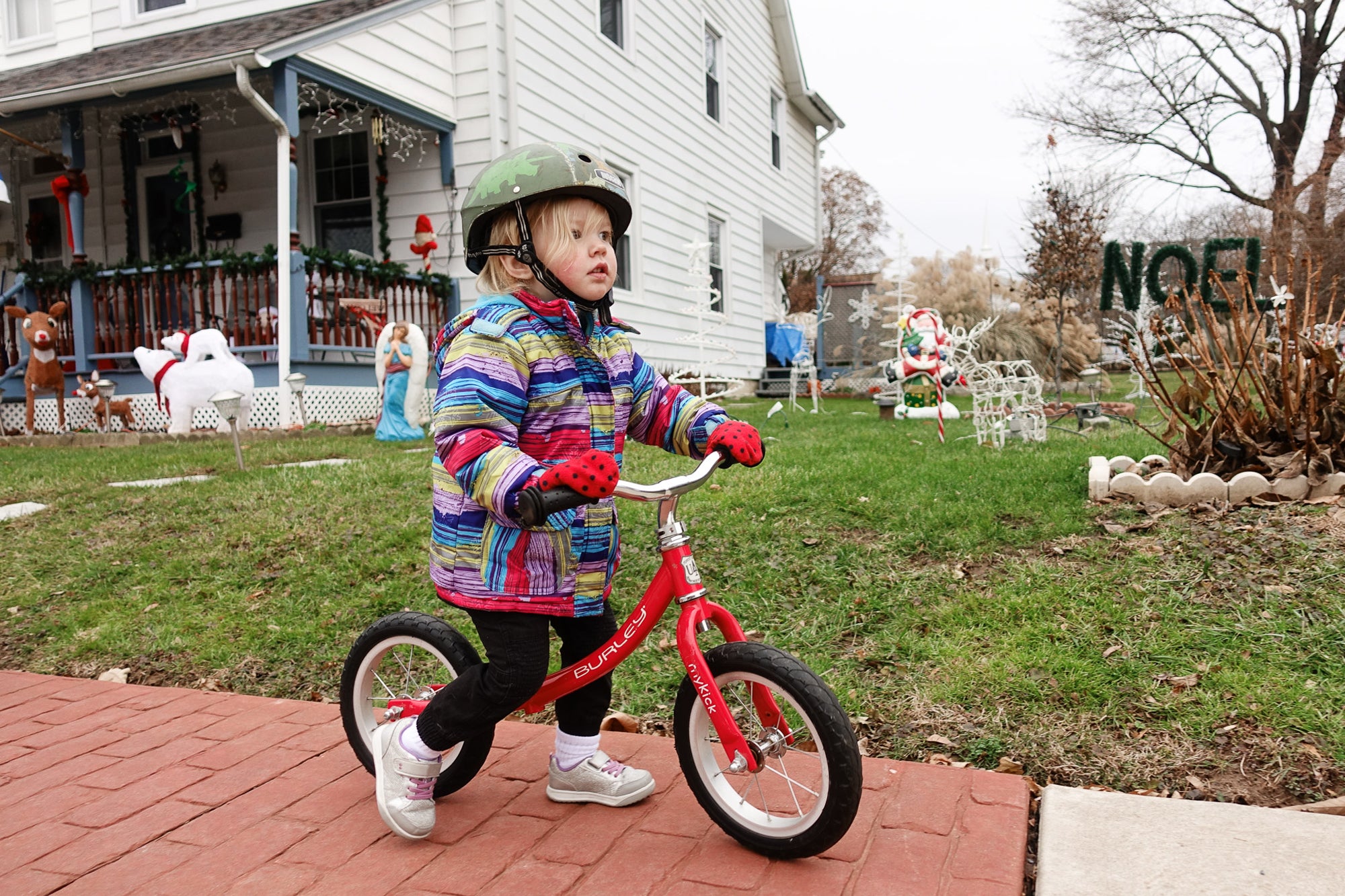 young girl and a balance bike walks down a brick driveway