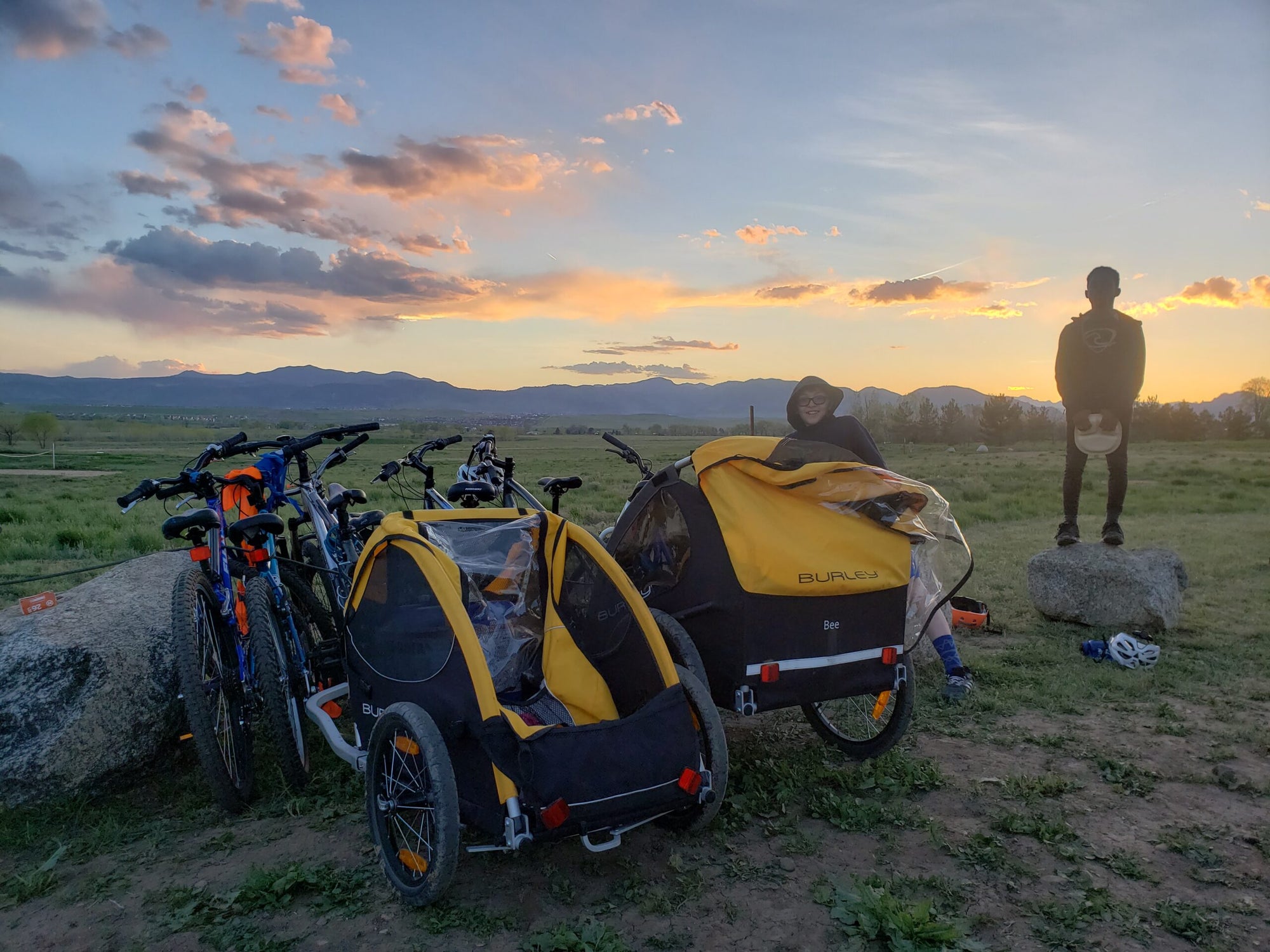 bike trailers and bikes parked in field with sunset in background