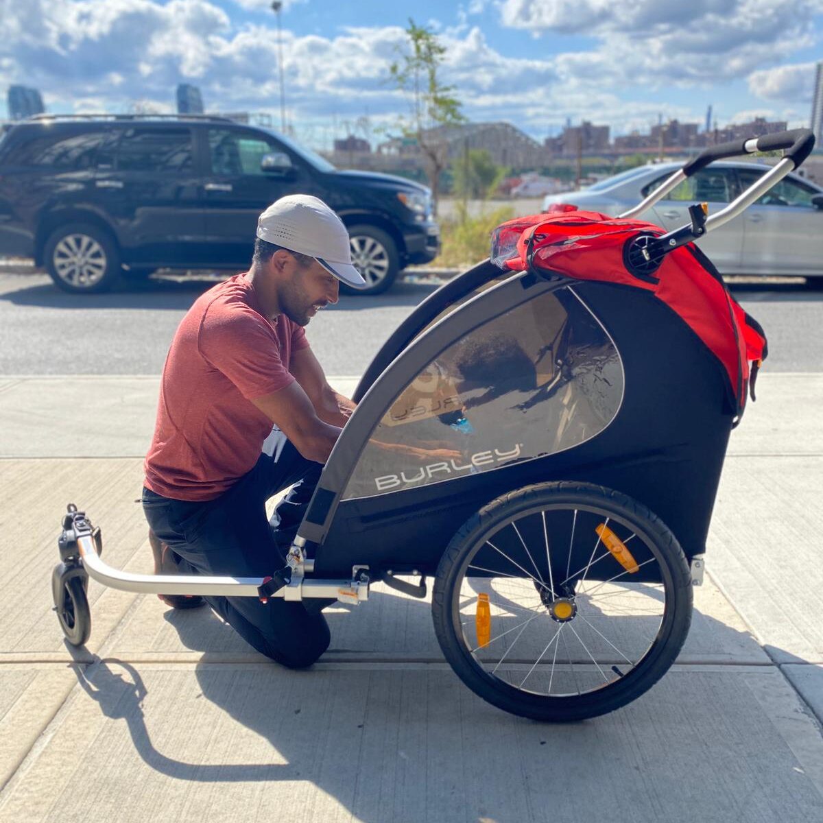 man kneeling down to buckle his son in to a kids bike trailer
