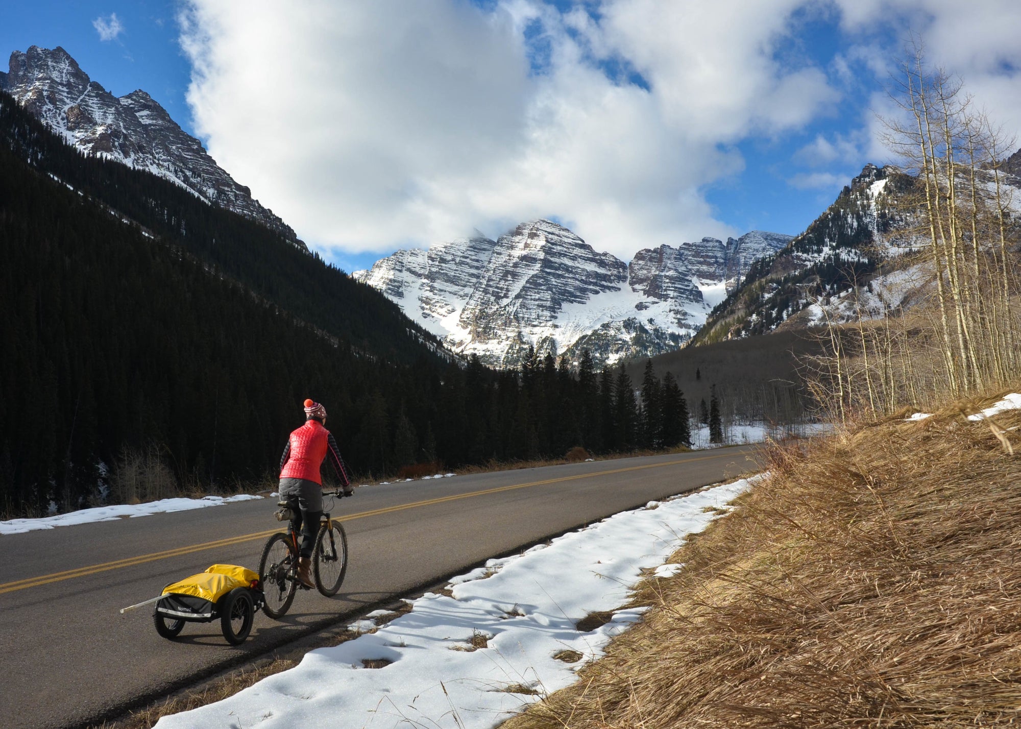 cyclist riding on mountain road with cargo bike trailer in tow. snowy mountain in background