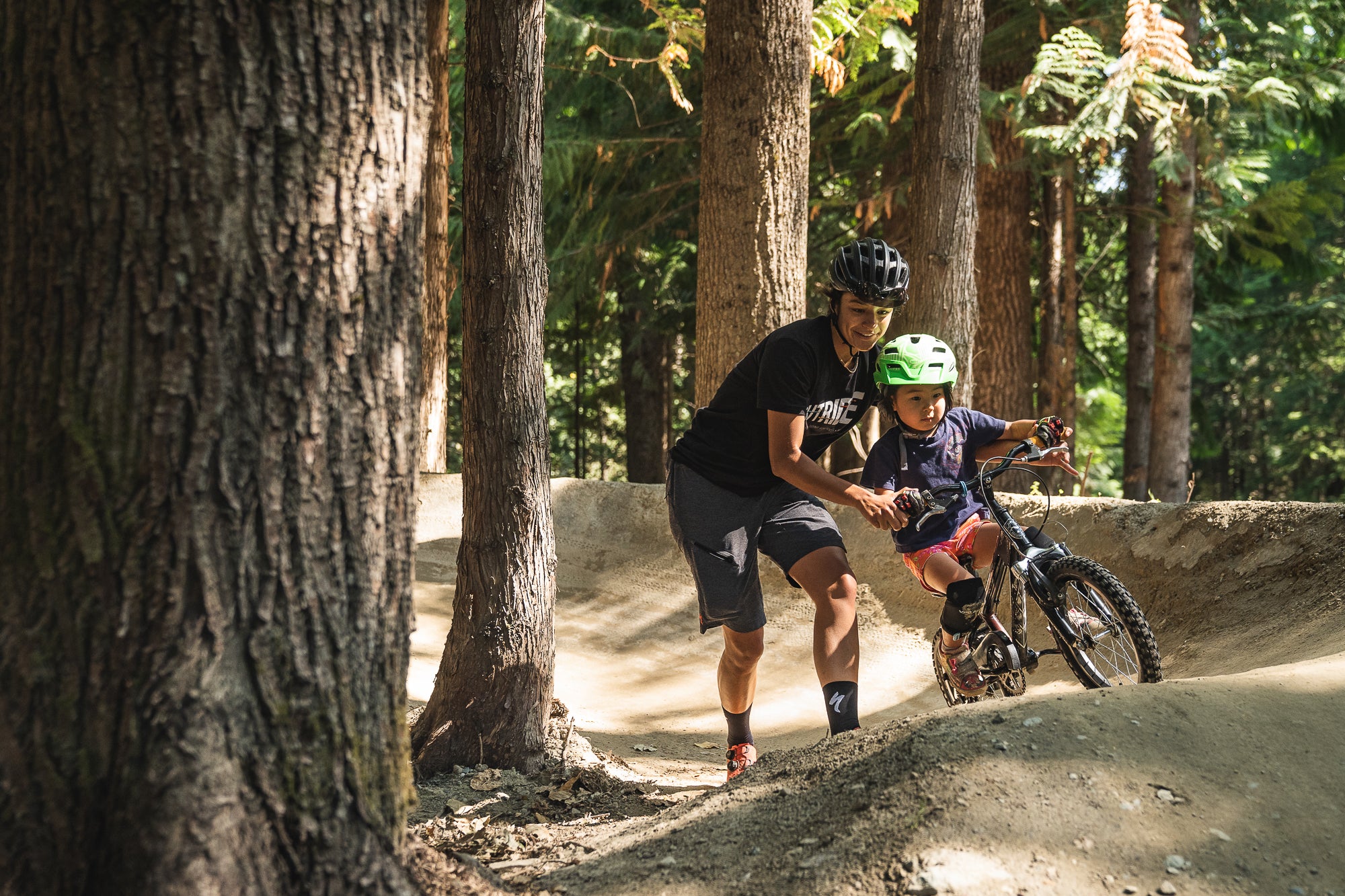 woman helping young kid ride bike over mountain bike course