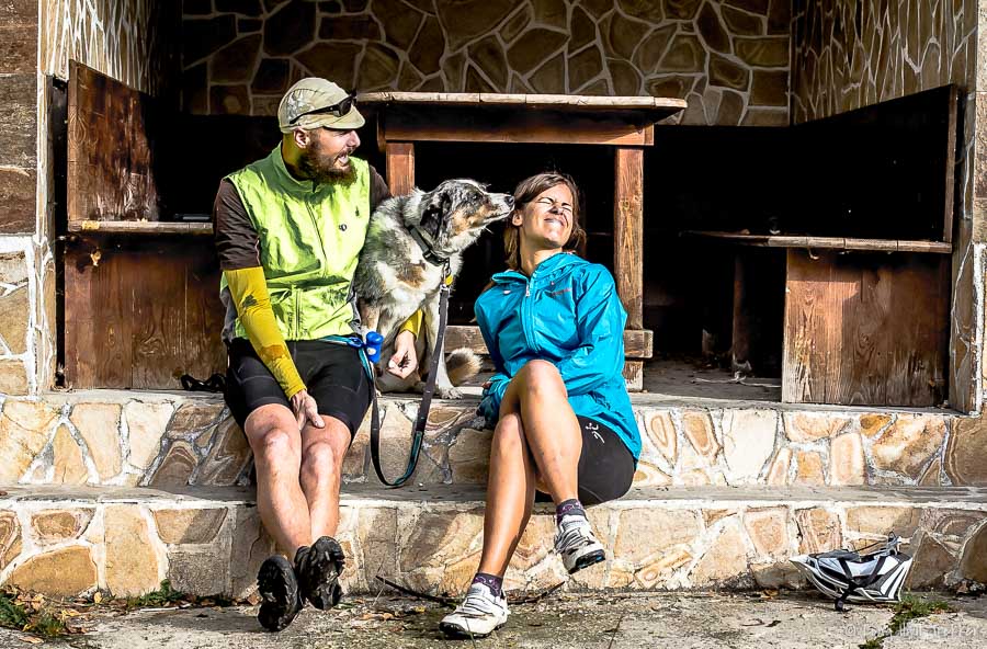 man and woman sit on stone steps with their dog. Dog is licking woman's face