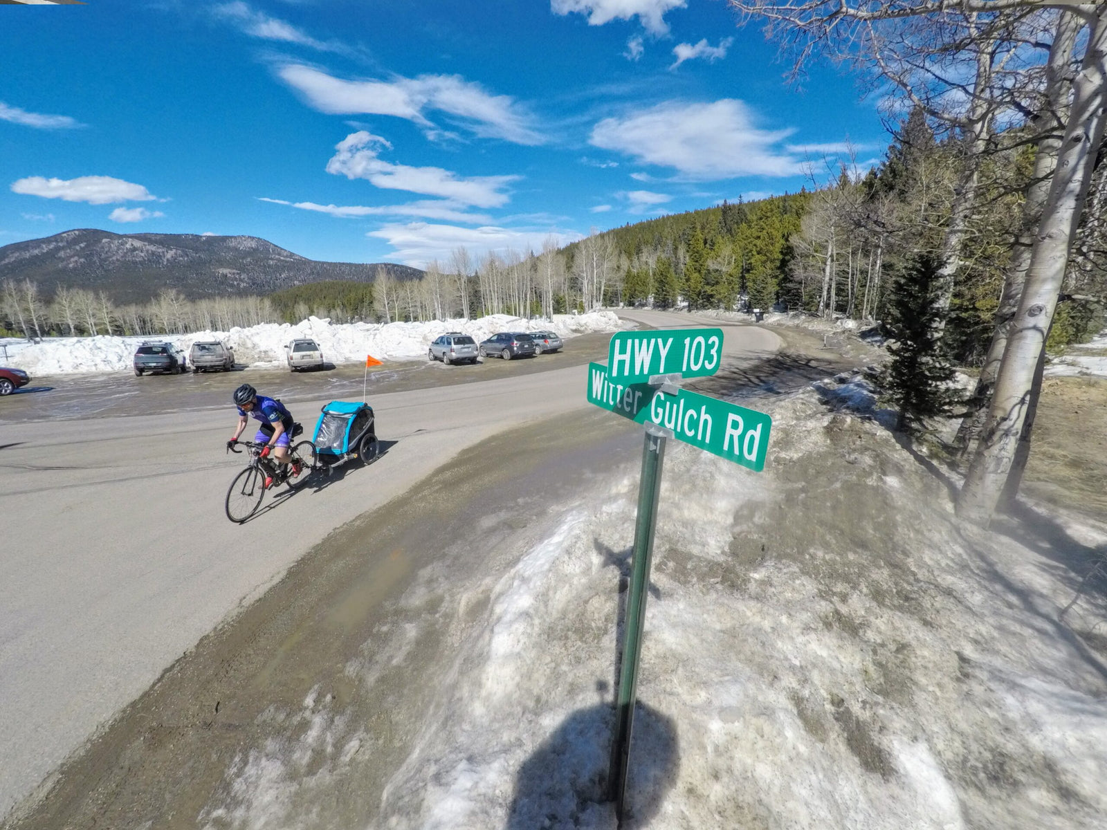 man biking up mountain pass with kids bike trailer attached to bike.