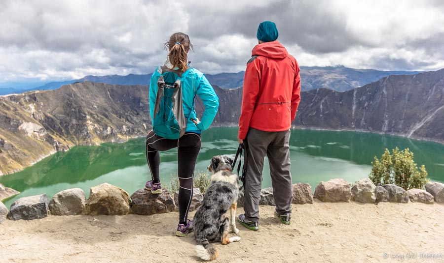 man and woman look out over a lake with dog sitting near them.