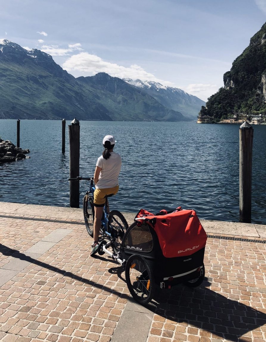 woman with bicycle and kid bike trailer looking out over Italian lake from cobblestone path