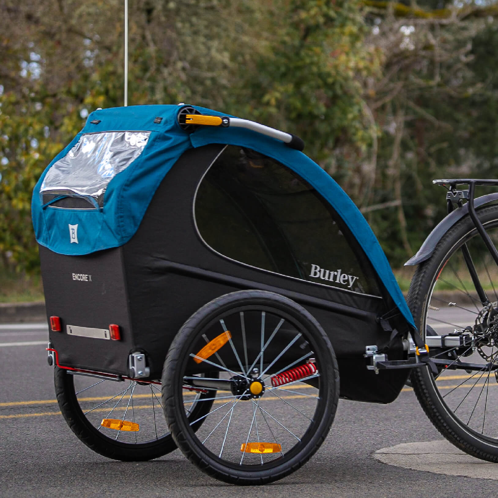 A Burley Encore X bike trailer for kids with a blue cover, black frame, and yellow accents. It has large wheels and is designed for versatility in different activities like biking, jogging, and skiing.