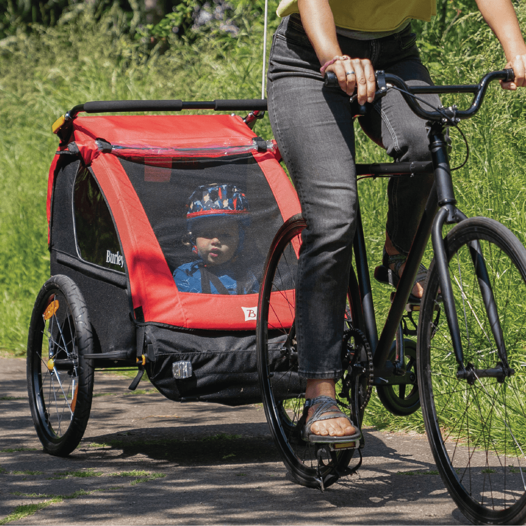 A red and black Honey Bee bike trailer-stroller hybrid with yellow accents, made from recycled materials, designed for biking and strolling with two kids.