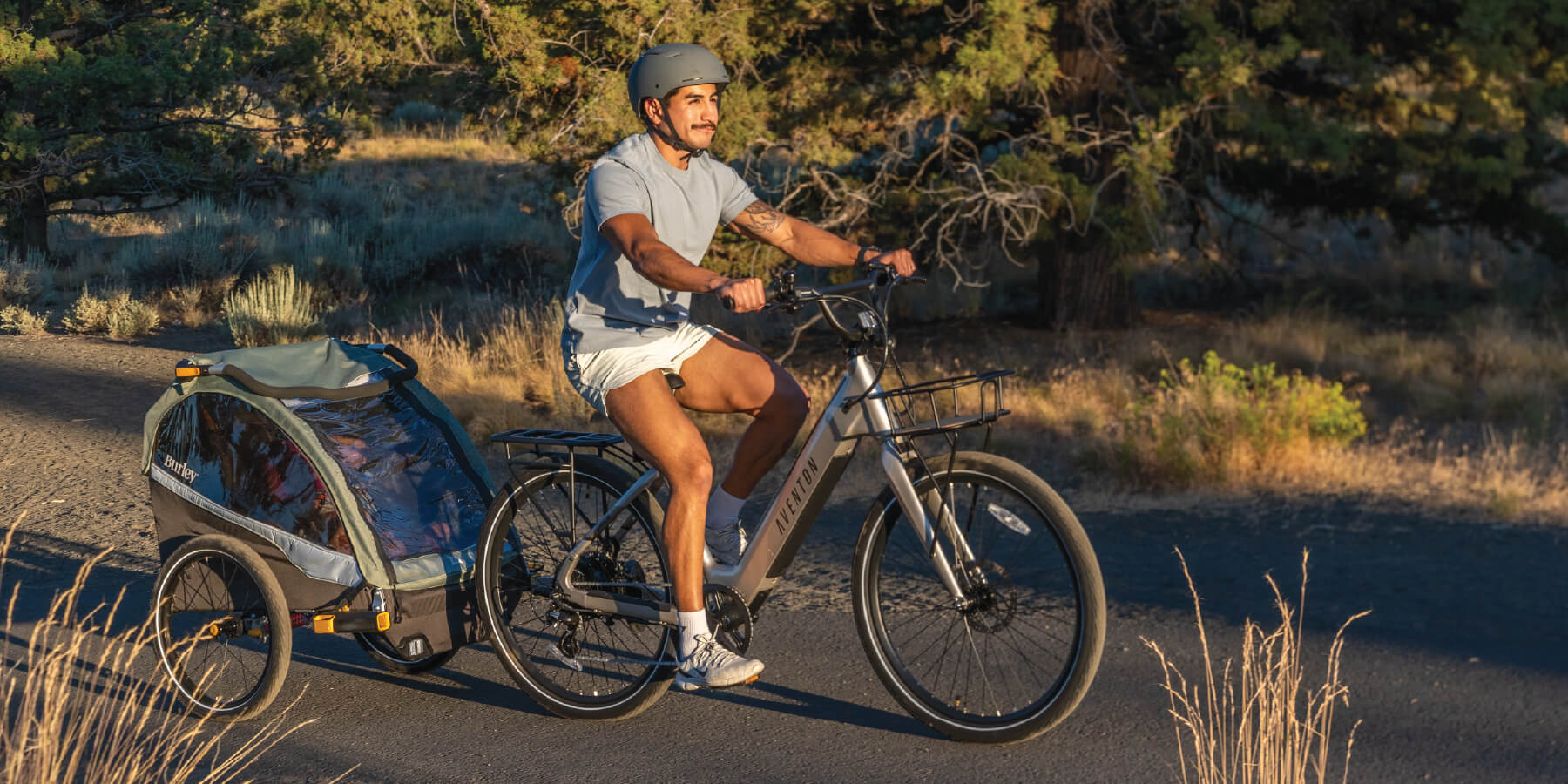 Father biking with kids in Burley D'LIte X kid trailer on wooded bike path.