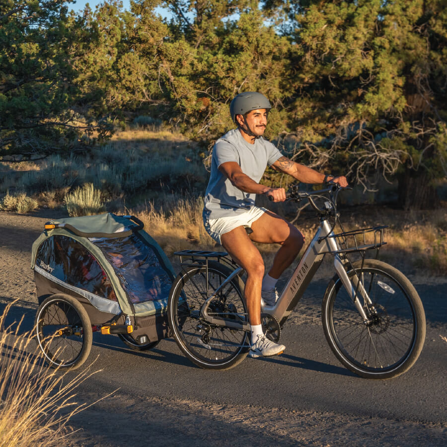 Father biking with kids in Burley D'LIte X kid trailer on wooded bike path.