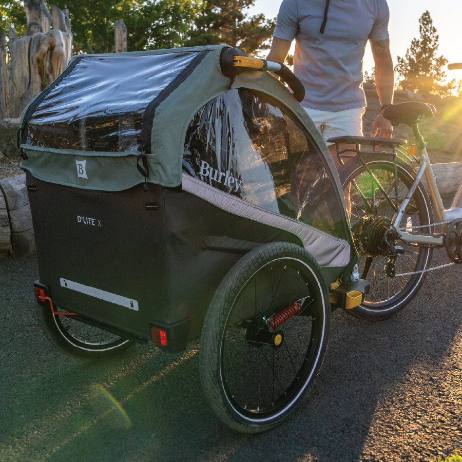 A sage green D'Lite X double bike trailer and stroller for kids with adjustable suspension and independently reclining seats, made with post-consumer recycled fabric.