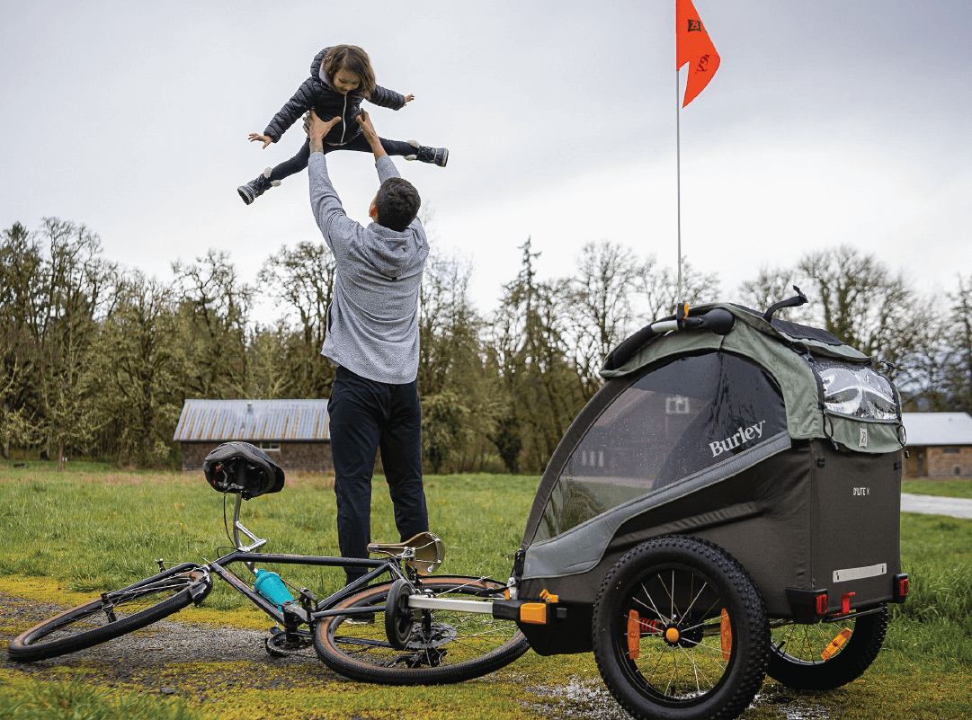 Father lifting child above head near Burley D'Lite X kid bike trailer