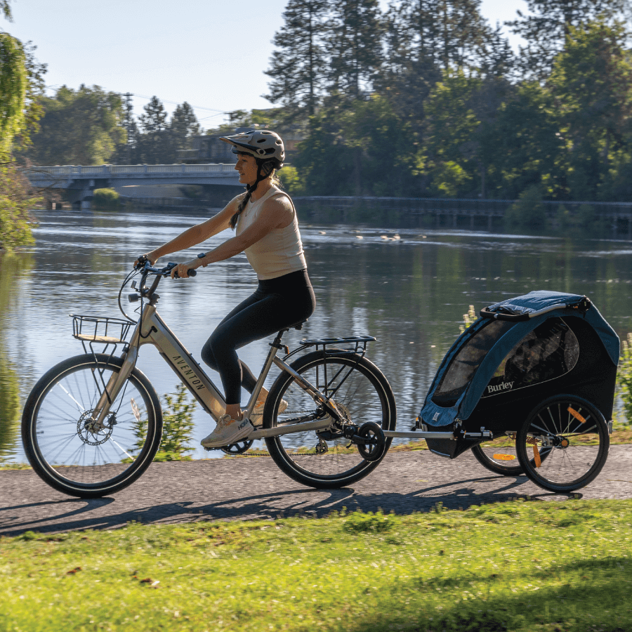 Parent riding a bicycle with Encore X child trailer by a lake
