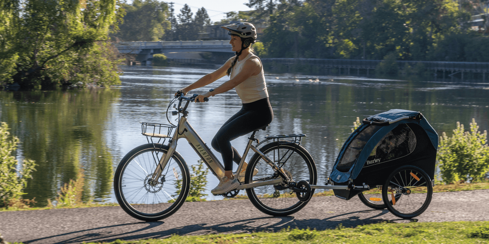 Parent riding a bicycle with Encore X child trailer by a lake