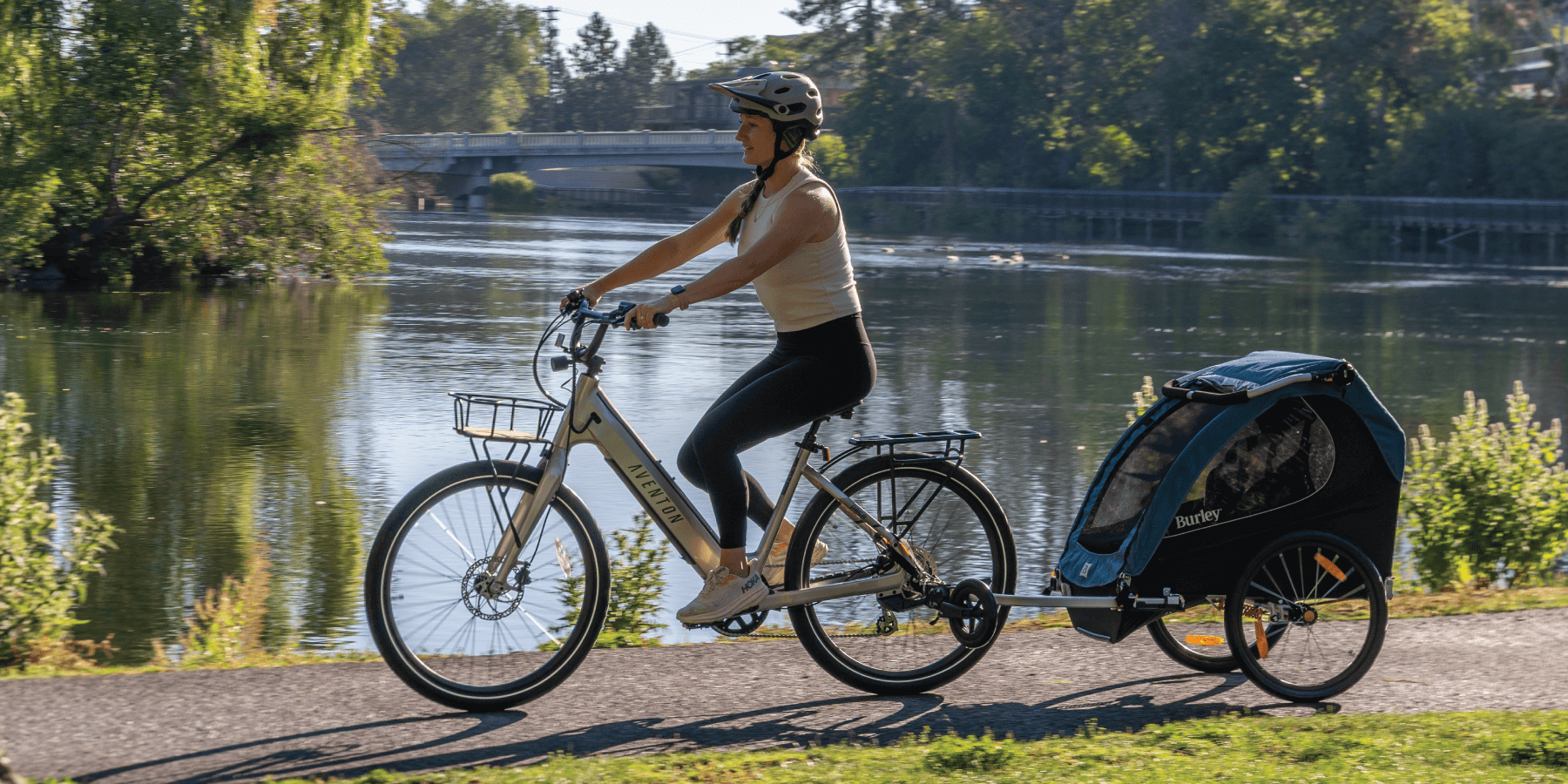 Parent riding a bicycle with Encore X child trailer by a lake