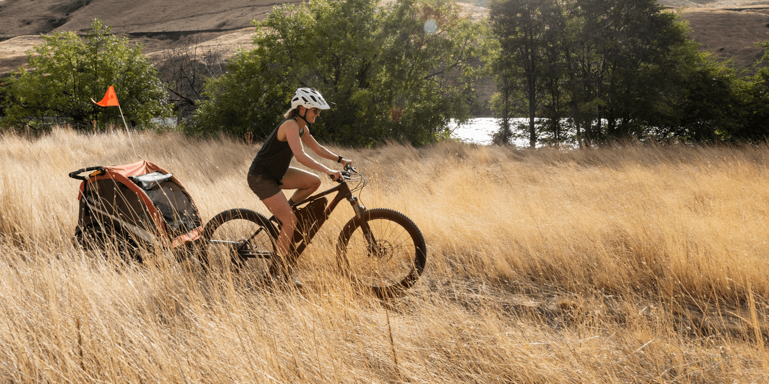 Mother biking with child in Burley Cub X trailer on wilderness trail